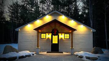 A wooden cabin with a front porch, a wreath, and a snow-covered ground.