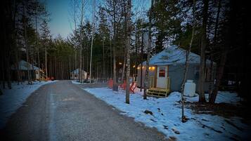 A snow-covered road leading to a cabin with a porch and a small shed.