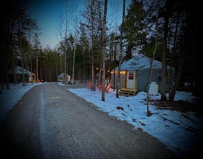 A snow-covered road leading to a cabin with a porch and a small shed. - The Rangeley Glamping Yurt in Bethel, Maine (Bethel)