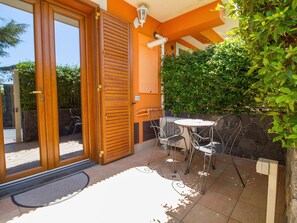 A patio with a table and chairs, a wooden door, and a wall with greenery. - Cozy Sicilian Family Stay (Trecastagni)