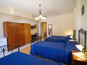 A bedroom with two beds, a wooden wardrobe, a desk with a chair, and a television on the wall. - Cozy Sicilian Family Stay (Trecastagni)