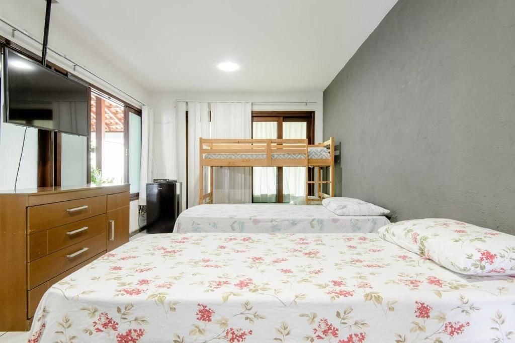 Une chambre avec un lit superposé, une commode en bois, un téléviseur et une fenêtre avec des rideaux.