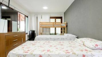 Une chambre avec un lit superposé, une commode en bois, un téléviseur et une fenêtre avec des rideaux.