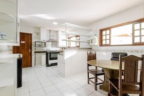 A kitchen with white cabinets, a stove, and a dining area with a table and chairs. - Pousada Queiroz (Rio de Janeiro)