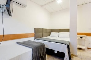 A hotel room with a single bed, a bedside table, and a wall-mounted air conditioning unit.