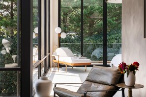 A modern room with large windows, a sofa, a chair, and a small table with a vase of flowers. - Amani Manor (Atlanta)