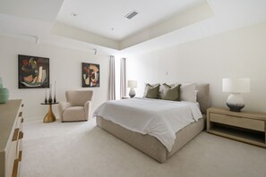 A modern bedroom with a large bed, a chair, a bedside table, and two wall-mounted paintings. - Amani Manor (Atlanta)