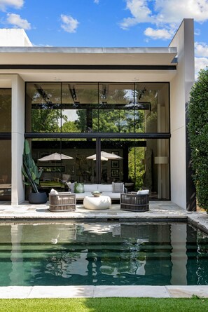 Une maison moderne dotée d’une piscine, d’un espace salon extérieur et de grandes fenêtres.