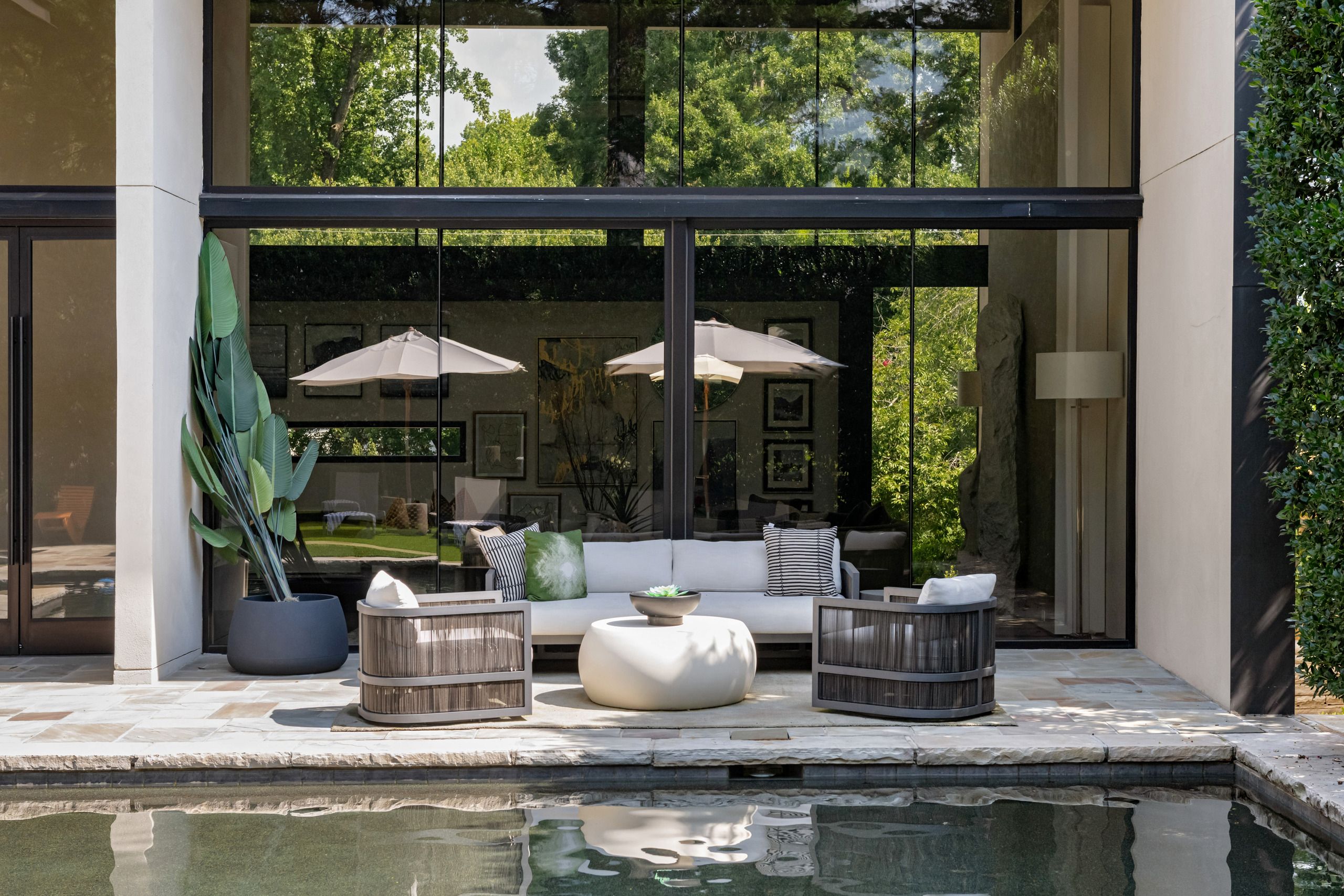 A modern outdoor seating area with a pool, featuring a sofa, two armchairs, and two umbrellas.
