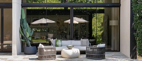 A modern outdoor seating area with a pool, featuring a sofa, two armchairs, and two umbrellas.