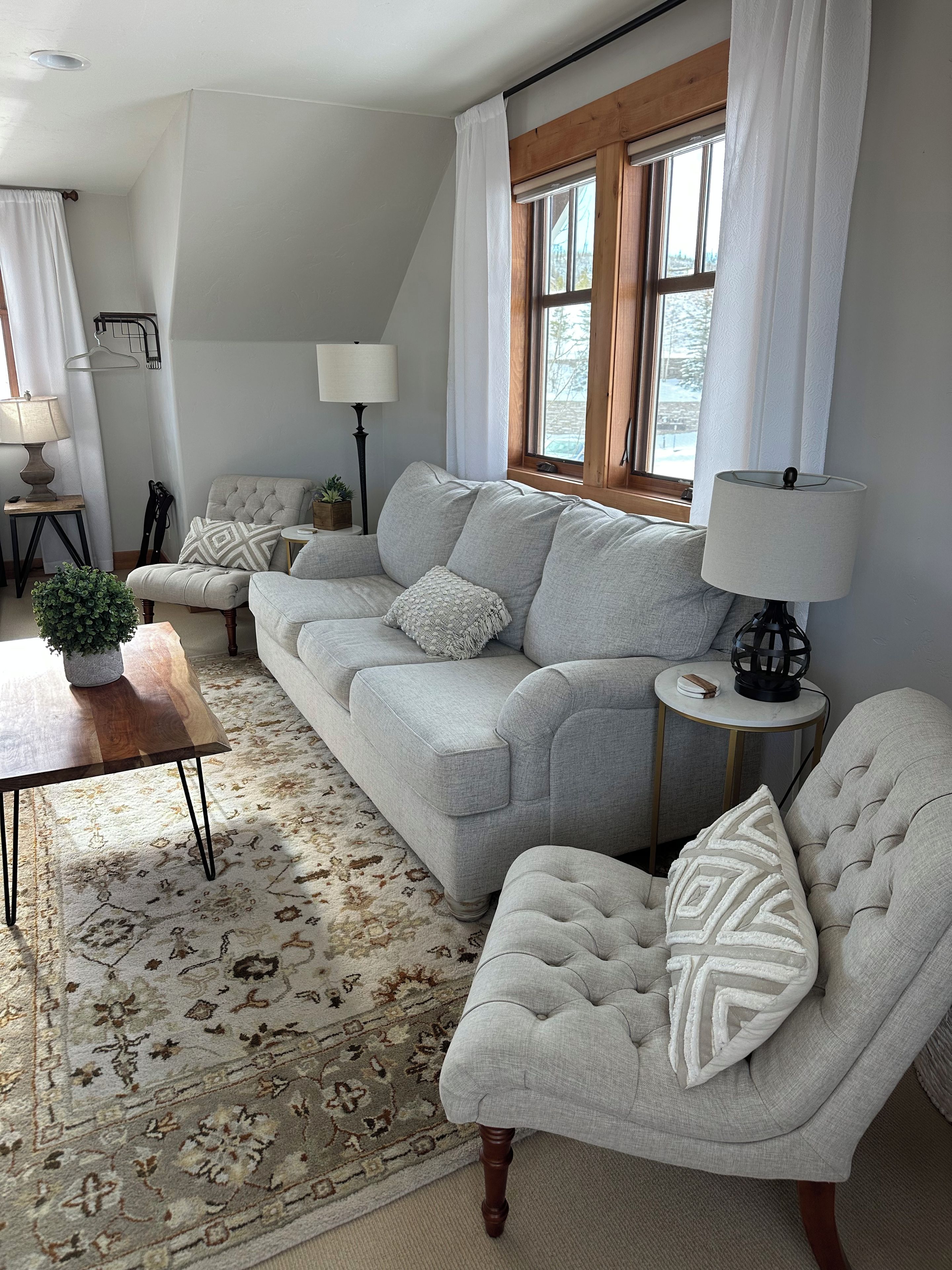 Ein Wohnzimmer mit einer Couch, einem Sessel, einem Beistelltisch, einer Lampe und einem Teppich.