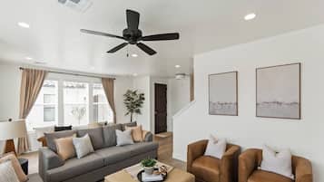 A modern living room with a grey sofa, brown armchairs, a ceiling fan, and two abstract paintings on the wall.