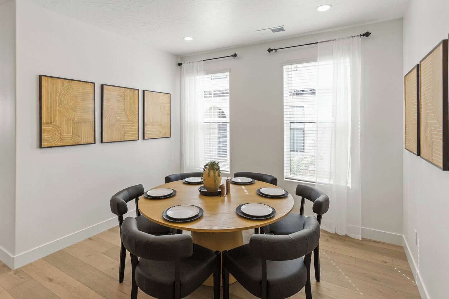 A dining area with a round table, six chairs, and three framed artworks on the wall.