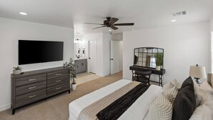 Ein Schlafzimmer mit Bett, Kommode, Fernseher, Schreibtisch, Stuhl und Deckenventilator.