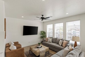 A modern living room with a flat-screen TV, a ceiling fan, a sofa set, and a coffee table. - Heated Pool, Pickle Ball, Spacious Home Close to National Parks (Washington)