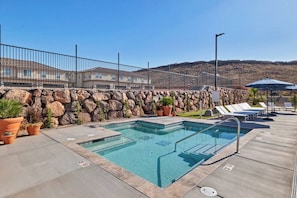 A pool area with a stone wall, lounge chairs, and potted plants. - Heated Pool, Pickle Ball, Spacious Home Close to National Parks (Washington)