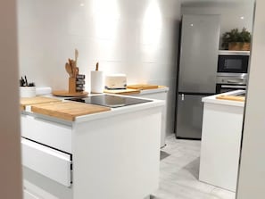 Ett modernt kök med vita skåp, en inbyggd ugn och ett kylskåp i rostfritt stål.