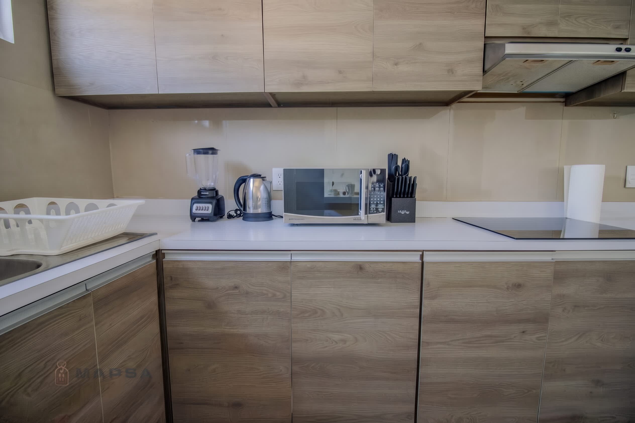 Une cuisine avec des meubles en bois, un four à micro-ondes, un mixeur et une bouilloire.