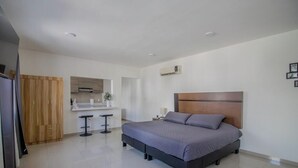 A bedroom with a bed, a wooden wardrobe, a small kitchen area, and a bathroom. - Comfortable King Loft in Apodaca - Ground Floor (Ciudad Apodaca)