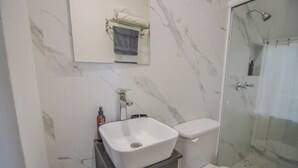 A bathroom with a marble wall, a white sink, a toilet, and a glass shower enclosure. - Comfortable King Loft in Apodaca - Ground Floor (Ciudad Apodaca)