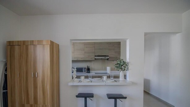 A modern kitchen with a built-in microwave, a white countertop, and two bar stools. - Comfortable King Loft in Apodaca - Ground Floor (Ciudad Apodaca)