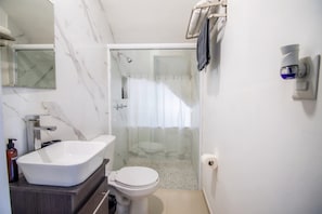 A bathroom with a marble wall, a white sink, a toilet, and a shower area.