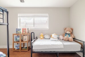A child's bedroom with a bunk bed, a bedside table with books, a teddy bear, and a window with blinds. - Private Home with Jacuzzi and Large Deep Pool close to NRG/Galleria/Downtown (Houston)