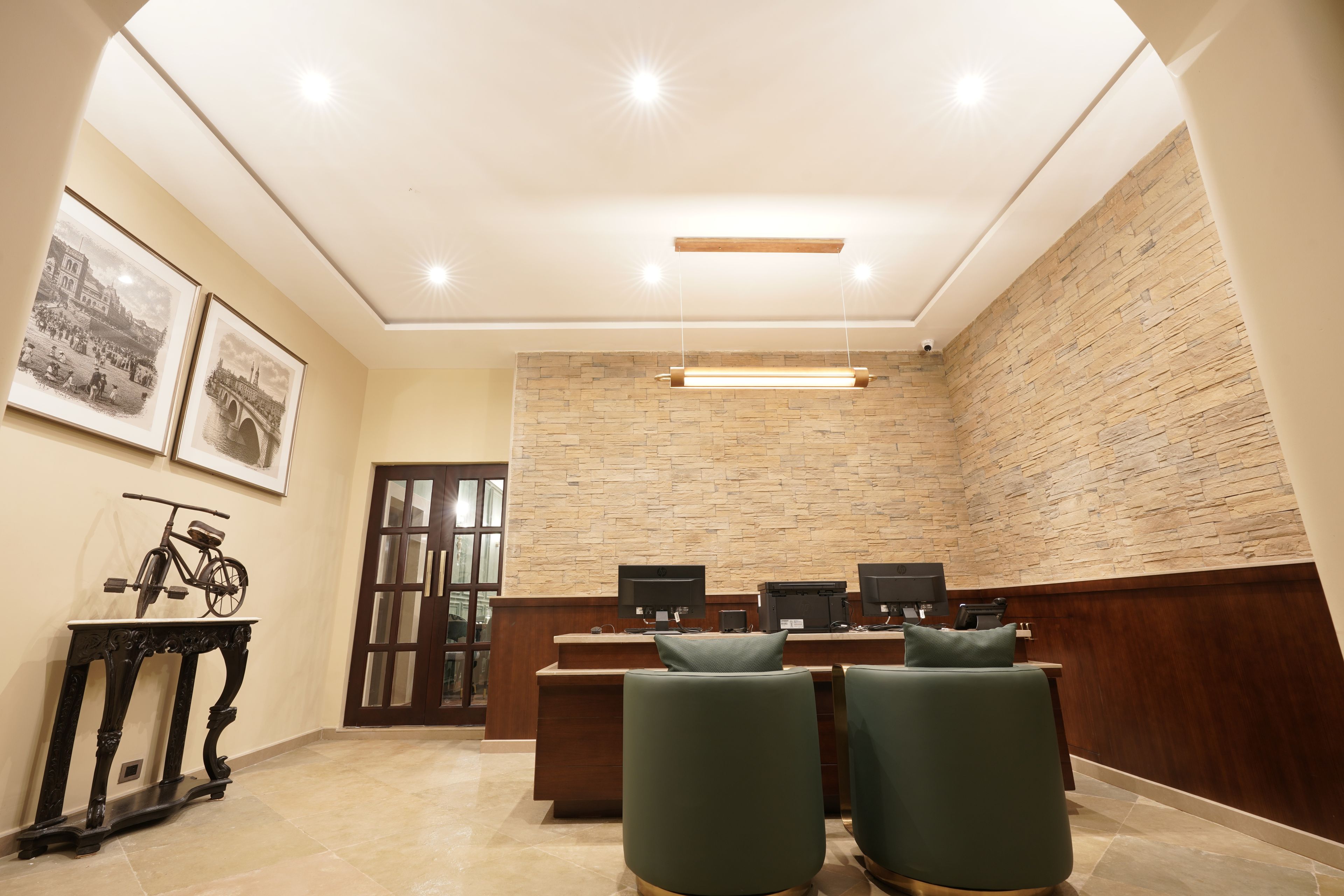 A conference room with a long table, two chairs, a desk with two monitors, and framed pictures on the wall.