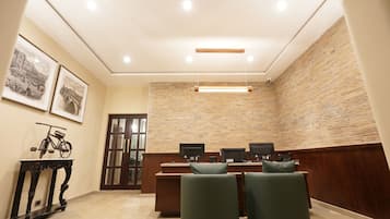 A conference room with a long table, two chairs, a desk with two monitors, and framed pictures on the wall.