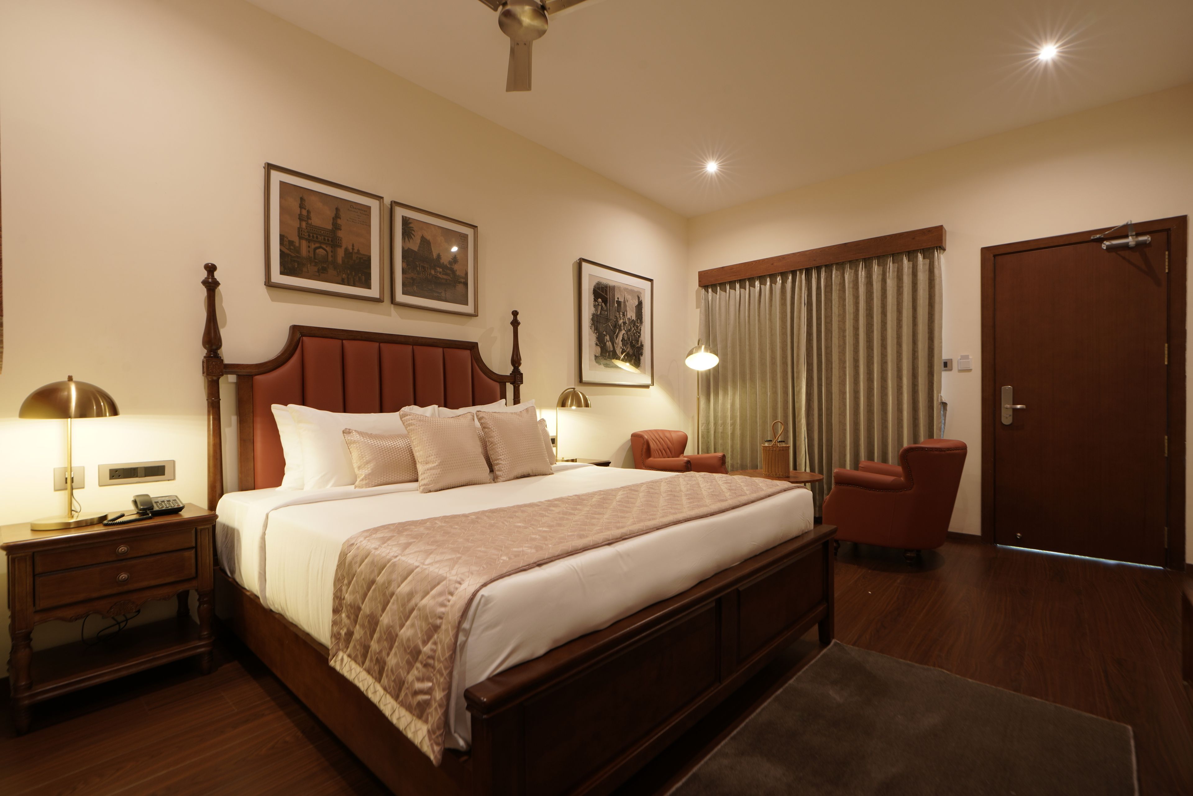 A hotel room with a large bed, bedside tables, a desk, a chair, a wardrobe, and a ceiling fan.