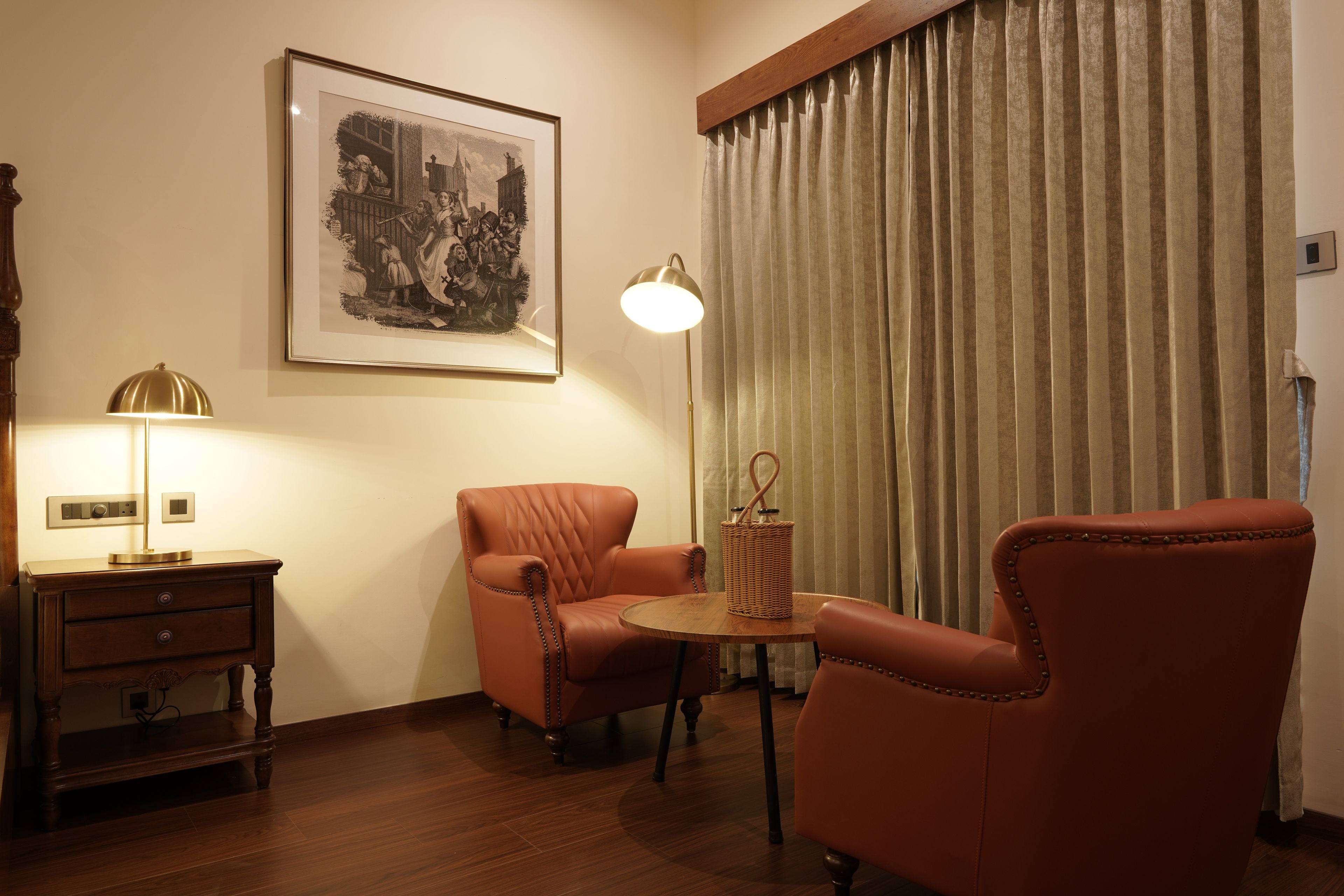 A room with a framed historical painting, a lamp, a wicker side table, and two leather armchairs.