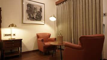 A room with a framed historical painting, a lamp, a wicker side table, and two leather armchairs.
