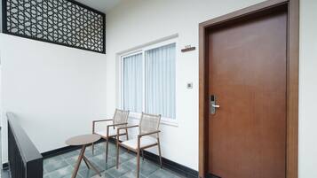 A room with a wooden door, a window with curtains, and two chairs.