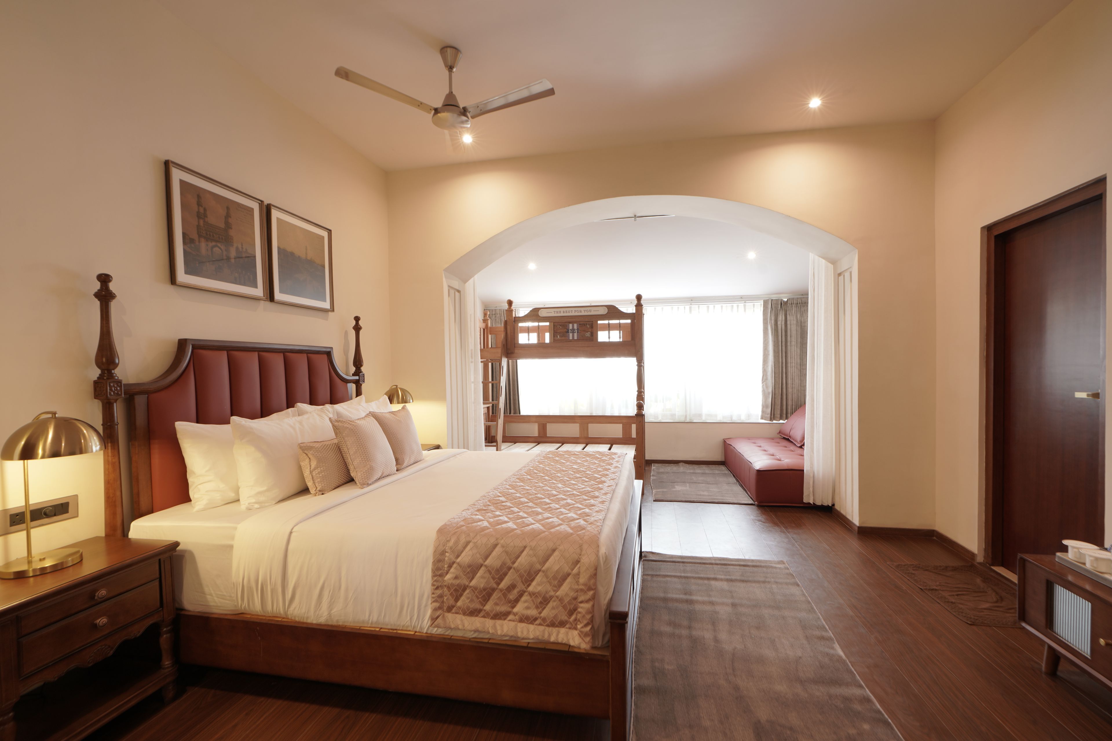 A hotel room with a large bed, a desk, a chair, a wardrobe, a ceiling fan, and a view of the outside.