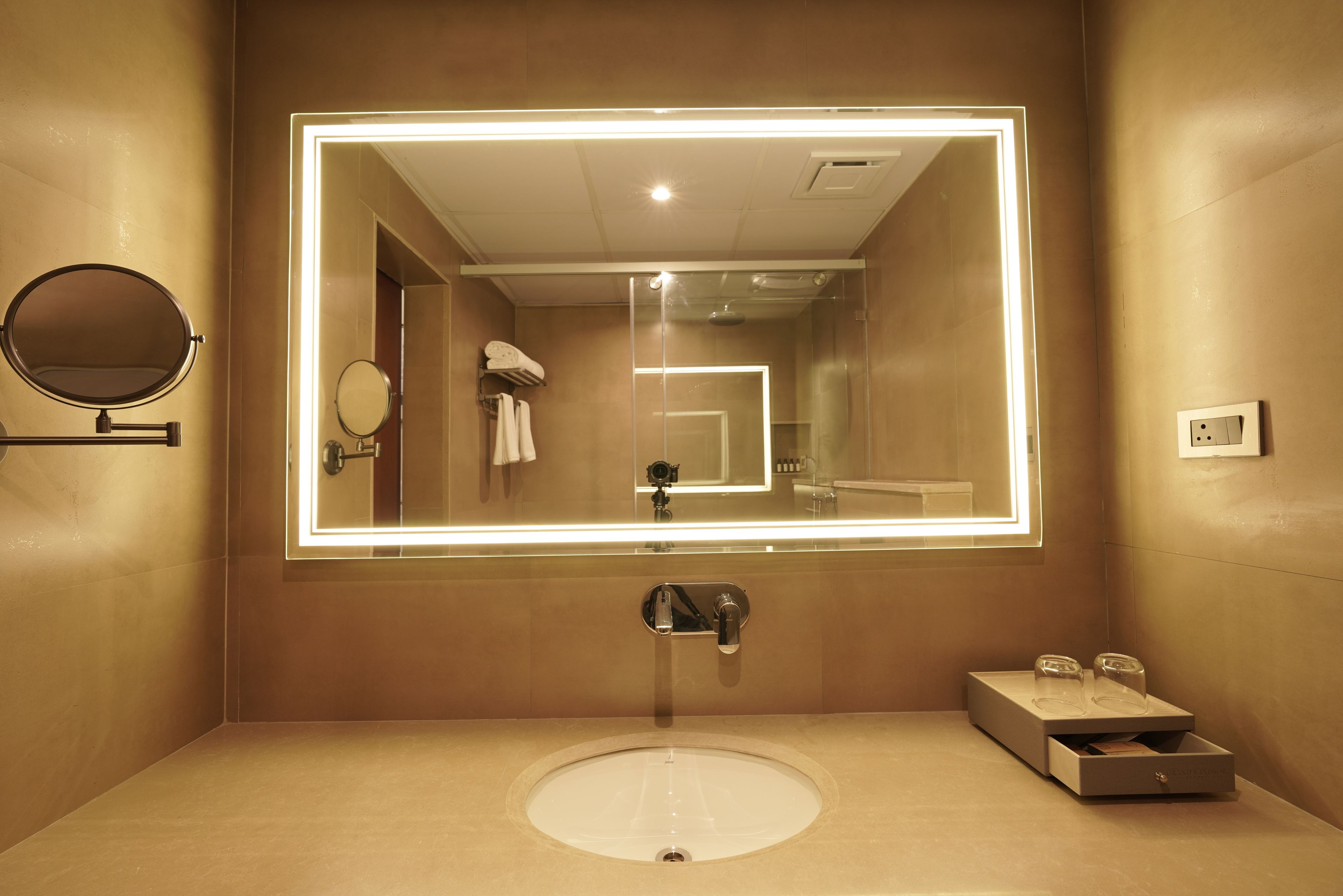 A bathroom with a large mirror, a round mirror, a sink, and a towel rack.