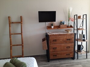 A room with a bed, a wooden dresser with drawers, a television mounted on the wall, and a shelving unit with various items. - Turquoise Studio, ocean view (Le Diamant)