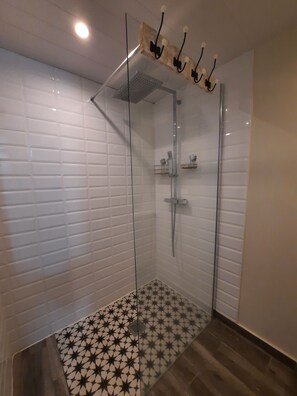 A glass-enclosed shower with a tiled floor, a ceiling-mounted light fixture, and a wall-mounted shelf. - Turquoise Studio, Ocean View (Le Diamant)