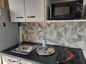 A kitchen with a stainless steel sink, a microwave, and a tray with a bottle, glasses, and a lime. - Turquoise Studio, ocean view (Le Diamant)
