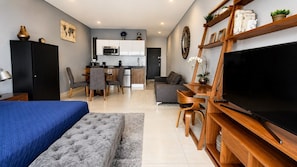 A modern living room with a large flat-screen TV, a sofa, a coffee table, and a dining area with chairs and a kitchen in the background. - Condesa Loft w/ Balcony, Fast WiFi & Jacuzzi (Mexico City)