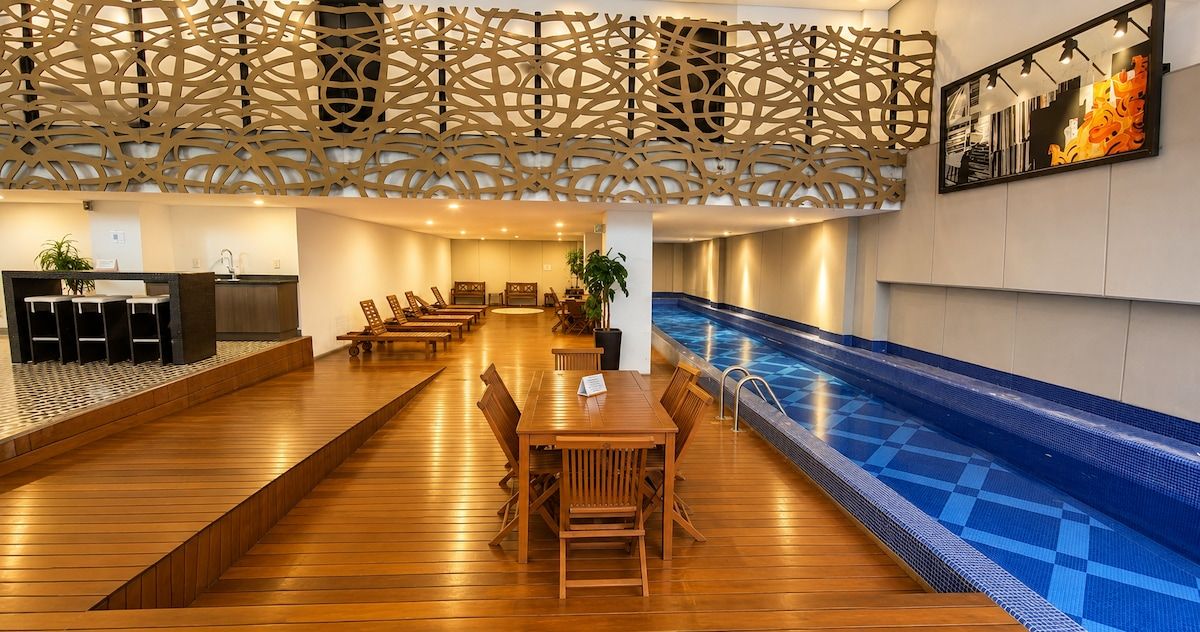 A hotel lobby with a pool, wooden flooring, a reception desk, and seating areas.
