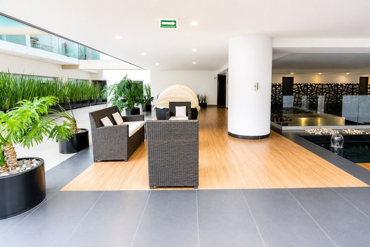 A modern lobby with a seating area, potted plants, and a water feature.