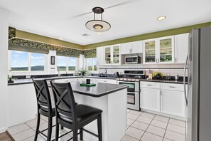A modern kitchen with white cabinets, a central island with bar stools, a stainless steel refrigerator, and a view of the outdoors.