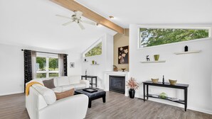 A modern living room with a white sofa, a fireplace, and a large window with a view of trees.