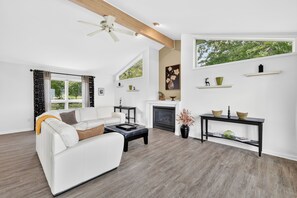A modern living room with a white sofa, a fireplace, and a large window with a view of trees.