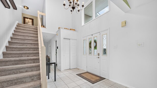 A staircase leading to a second floor, a chandelier, a set of double doors, and a tiled floor.
