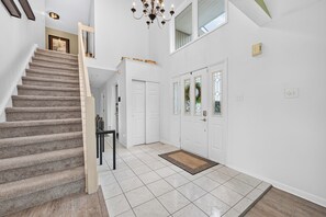 A staircase leading to a second floor, a chandelier, a set of double doors, and a tiled floor.