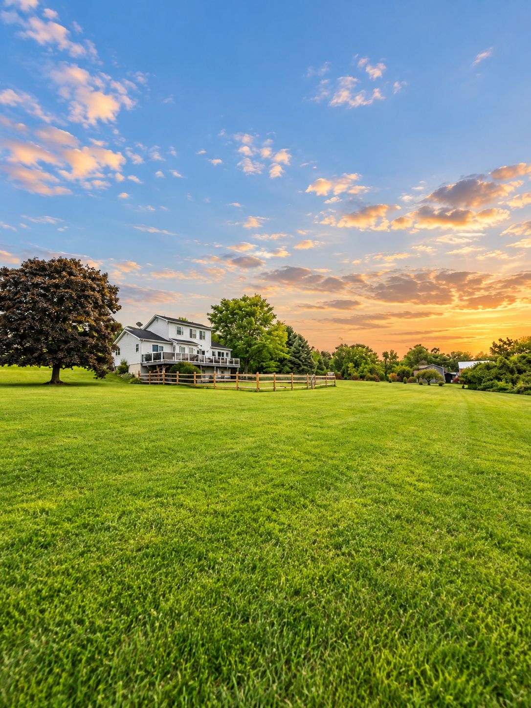 A large, open grassy field with a white house and a wooden fence in the background.