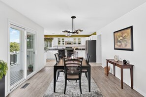 A modern kitchen with white cabinets, a dining area with a wooden table and chairs, and a large window with a view of greenery.