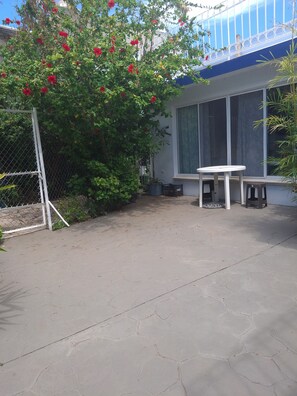 Eine Terrasse mit einem weißen Tisch und Stühlen, einem Zaun aus Maschendraht und einem Blumentopf.