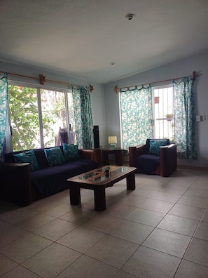 A living room with a sofa, two armchairs, a coffee table, and large windows with curtains. - PURPLE LOTUS COZUMEL (Cozumel)